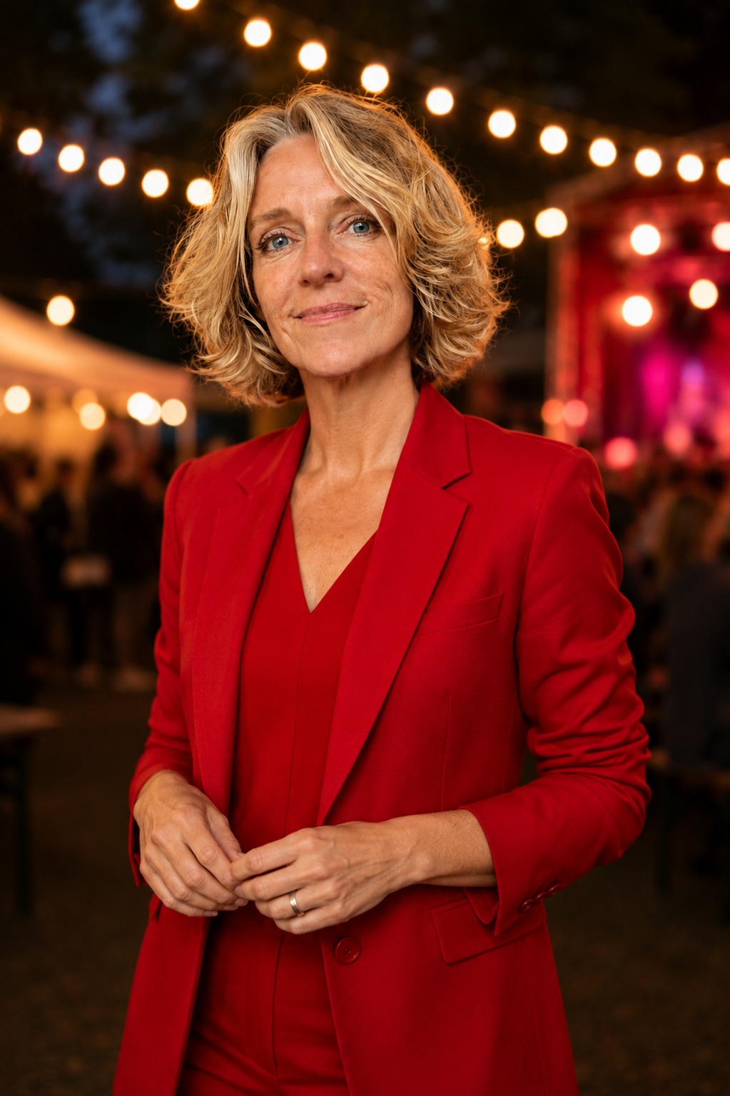 Anke Siegers in rood pak, met festivalverlichting op de achtergrond